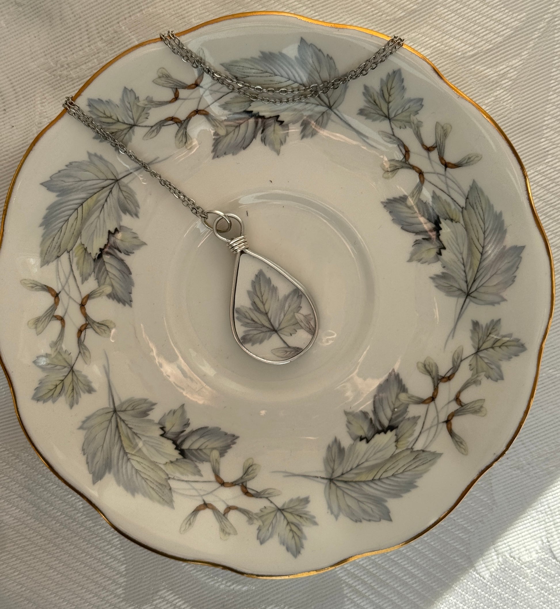 Teardrop-shaped pendant on a chain displayed on a decorative plate with leaf patterns.