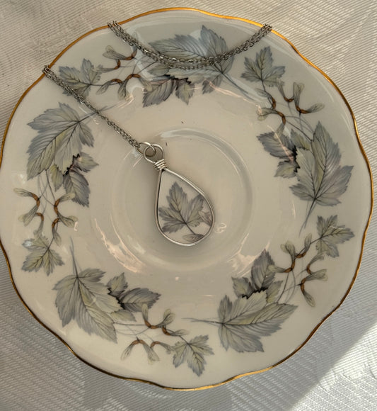 Teardrop-shaped pendant on a chain displayed on a decorative plate with leaf patterns.