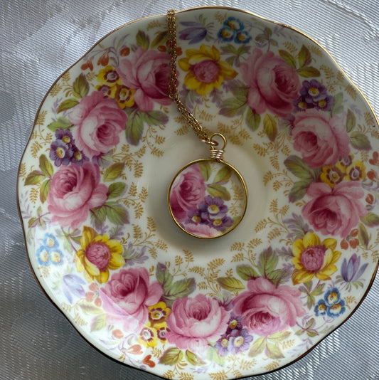 Decorative teacup with floral design and a matching necklace on a white lace background