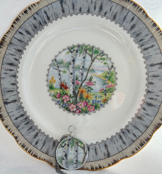 Decorative plate with nature-themed design and matching pendant on a white background