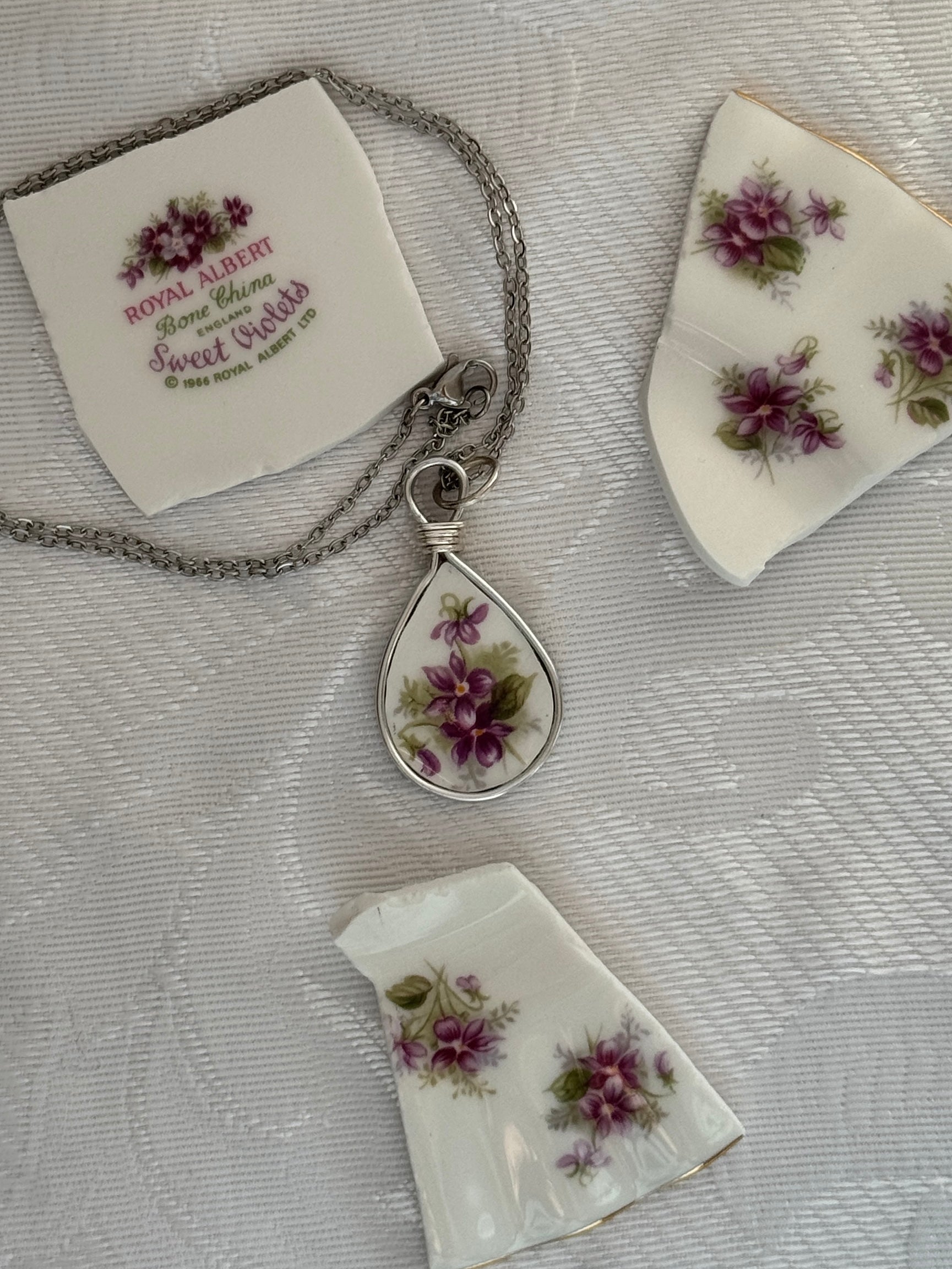Teardrop-shaped silver pendant with floral design on a textured surface