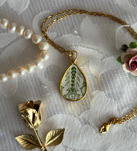 Gold necklace with a teardrop-shaped pendant on a textured white surface