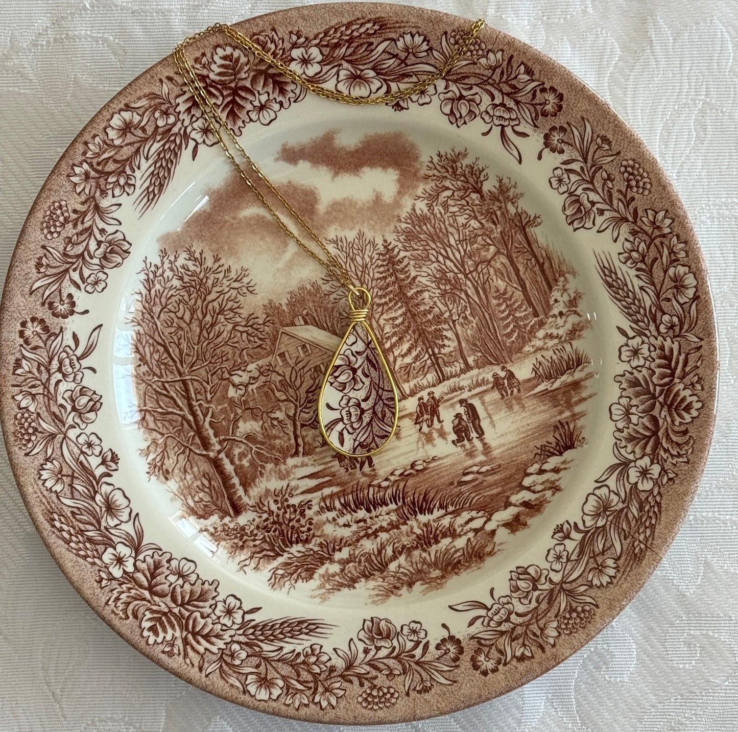 Decorative plate with a landscape design and a gold necklace on top