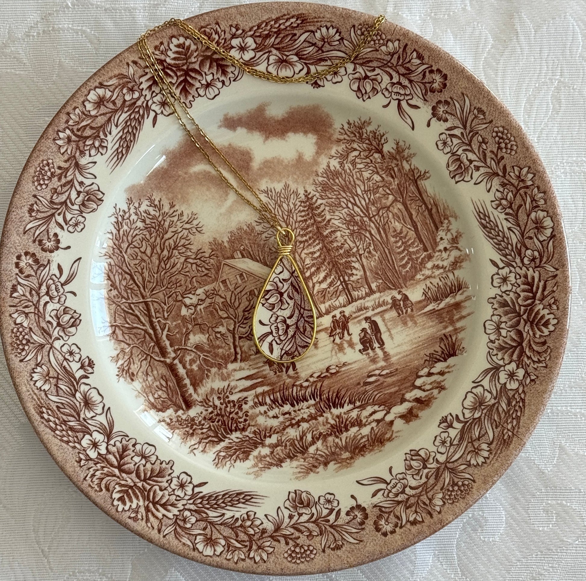 Decorative plate with a landscape design and a gold necklace on top