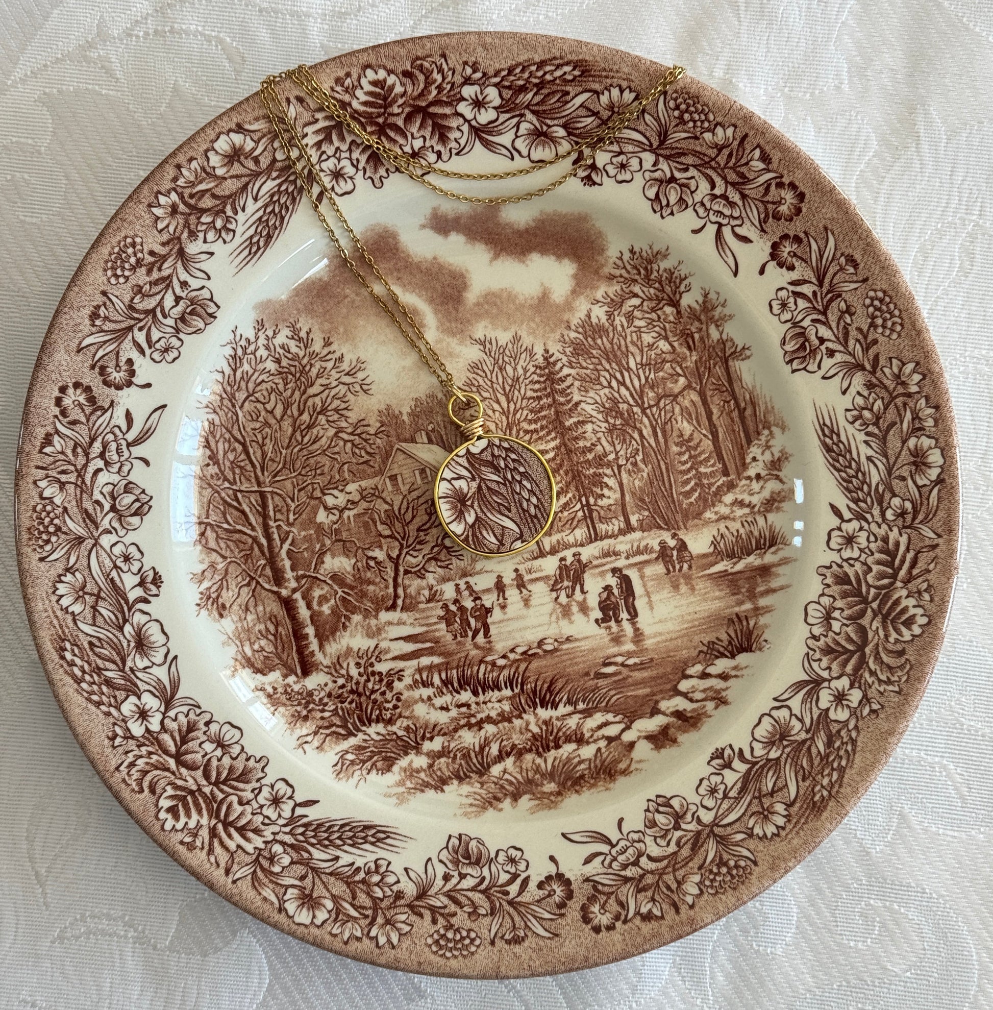 Decorative plate with a winter scene and floral border, featuring a necklace.