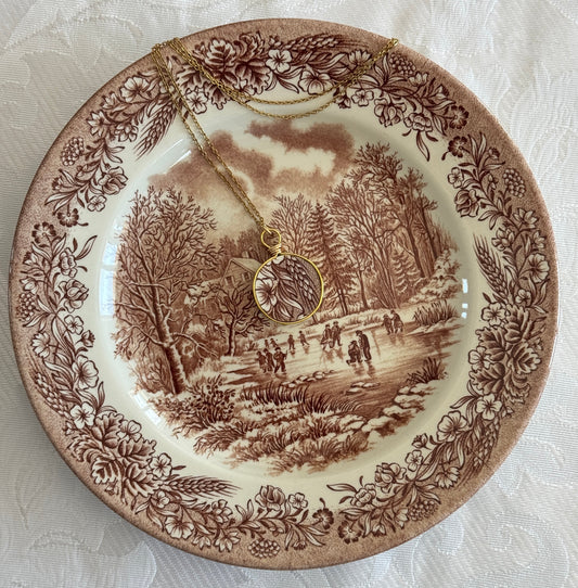 Decorative plate with a winter scene and floral border, featuring a necklace.
