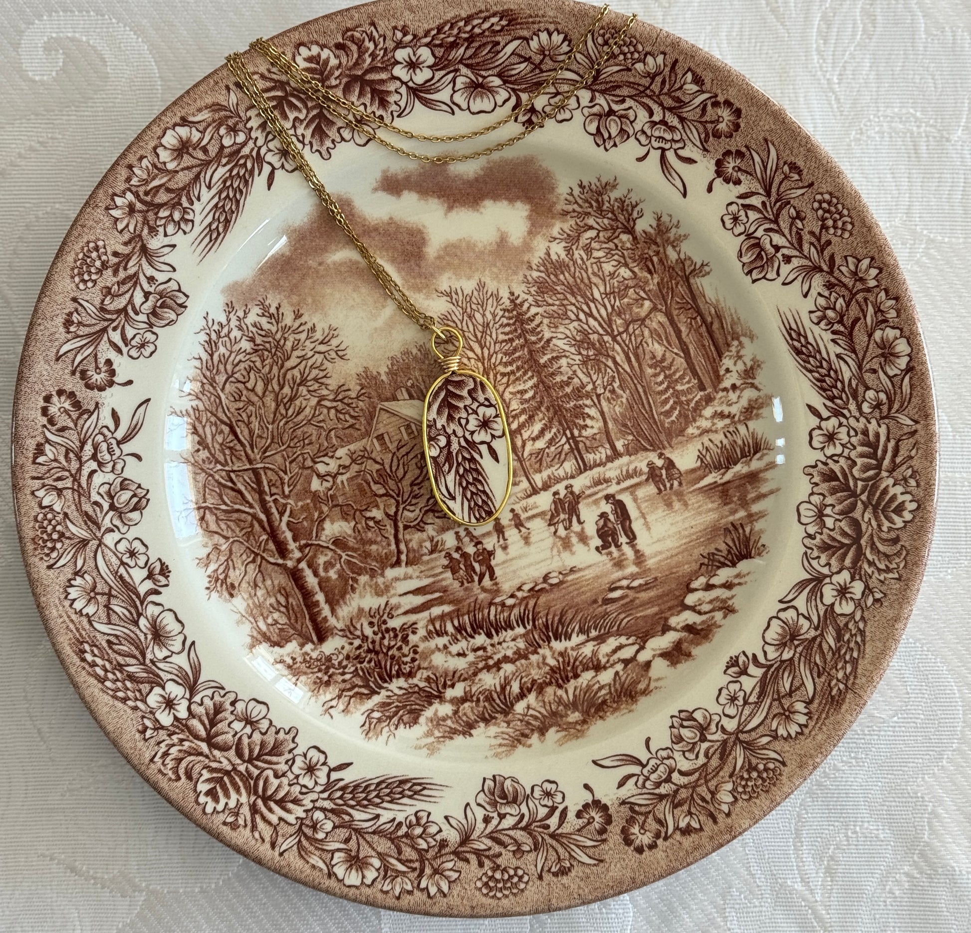 Decorative plate with a landscape design and a necklace draped over it on a textured surface.