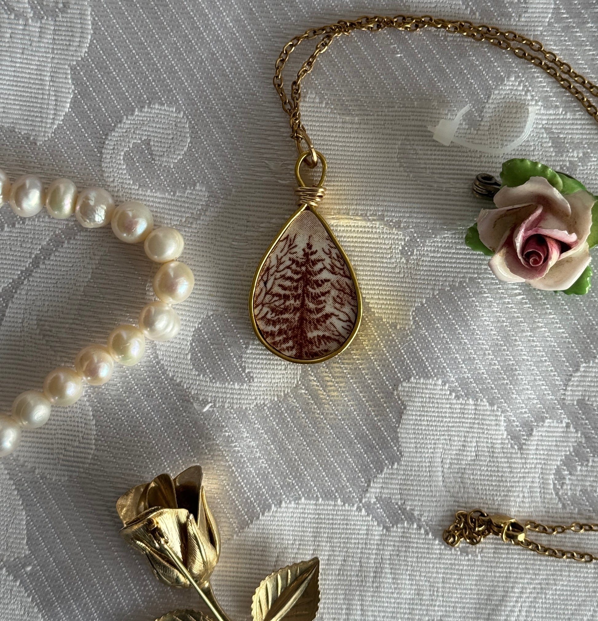 Gold necklace with a teardrop-shaped pendant with a tree on a textured white surface.