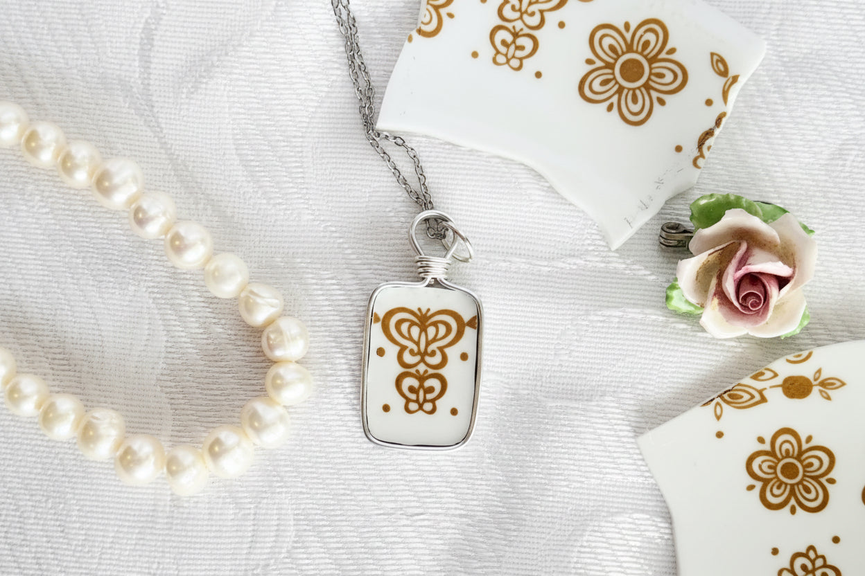Silver necklace with a Butterfly in gold pendant, pearl necklace, and floral rose on a decorative white surface.