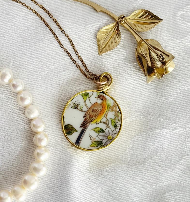 Gold necklace with a bird pendant and pearl bracelet on a textured white surface