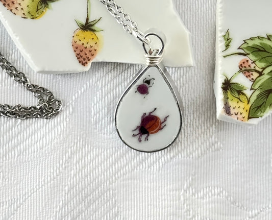 Teardrop-shaped pendant with two beetles on a white surface