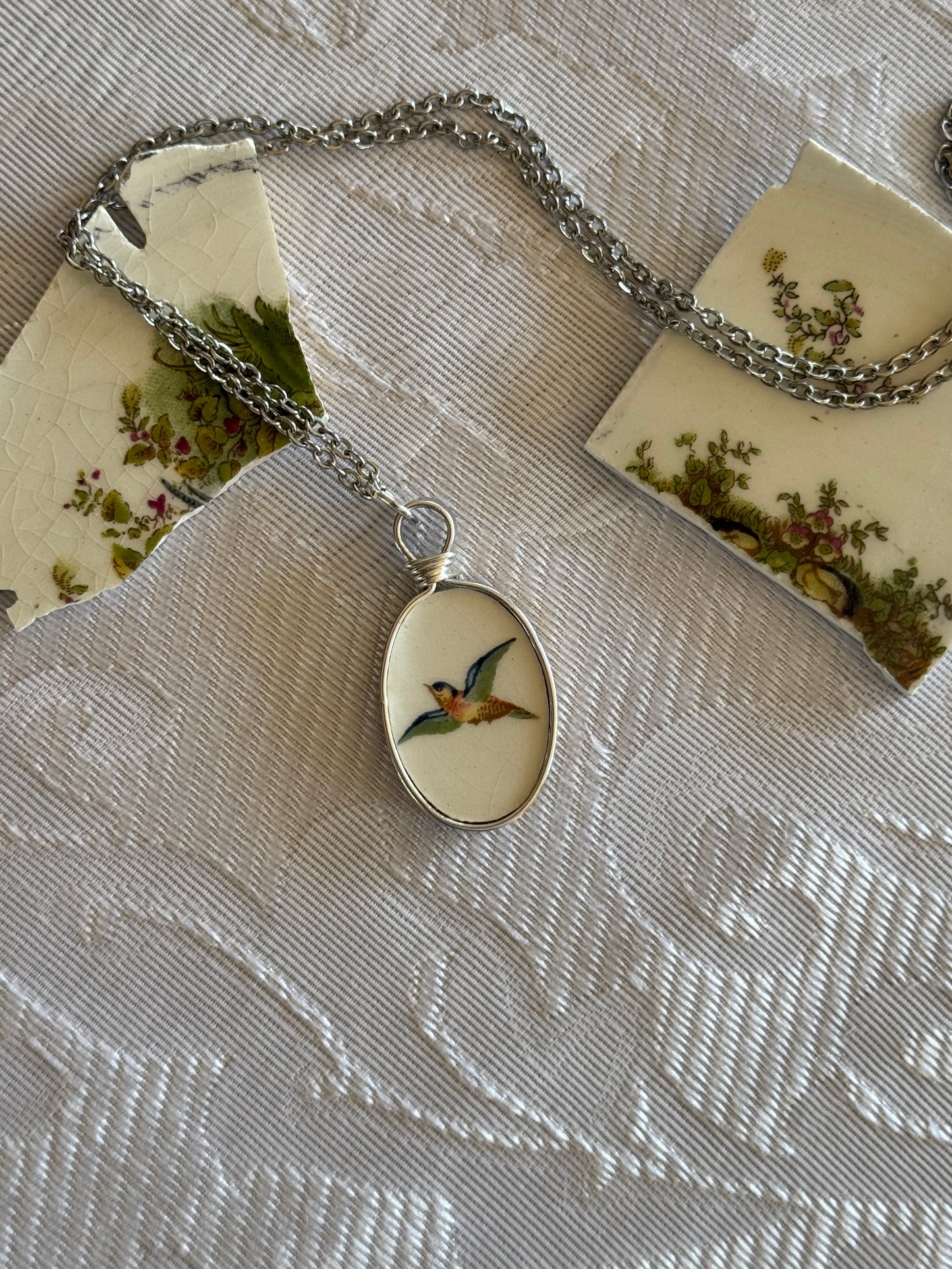 Necklace with a pendant featuring a bird design on a textured fabric background