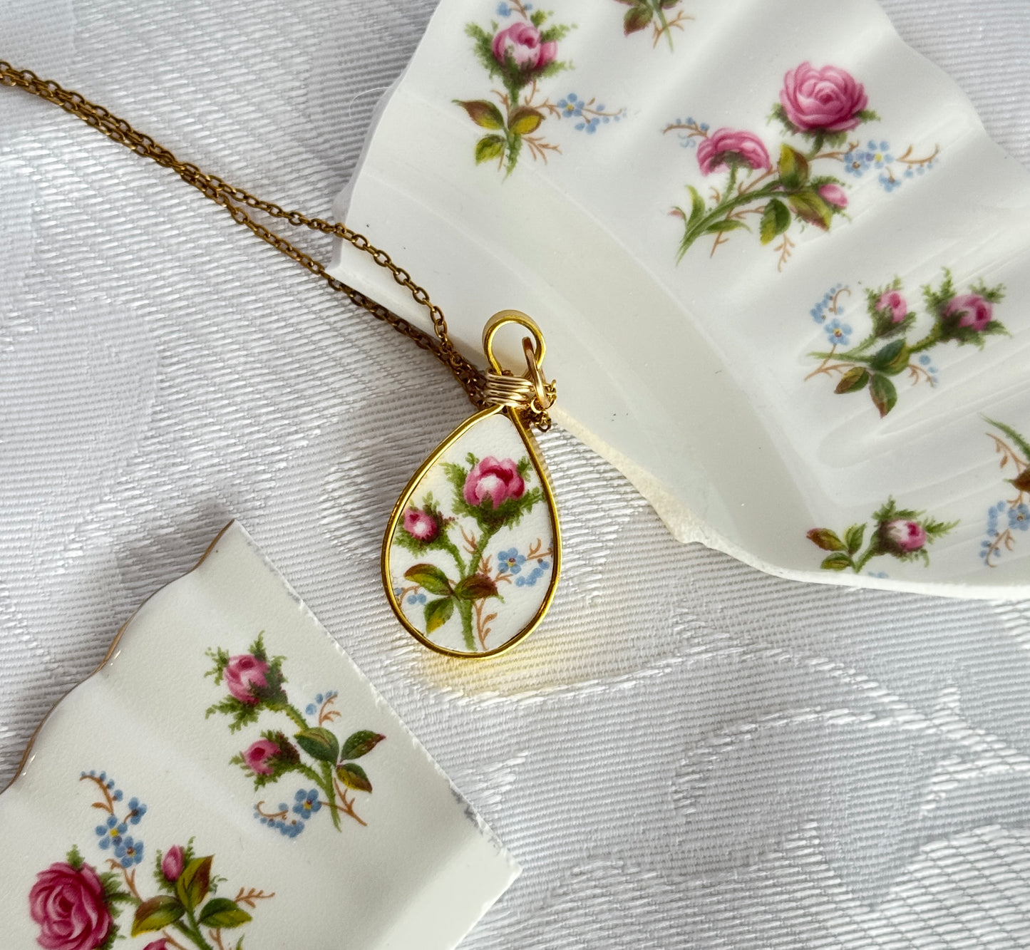 Teardrop-shaped pendant with floral design on a white fabric background