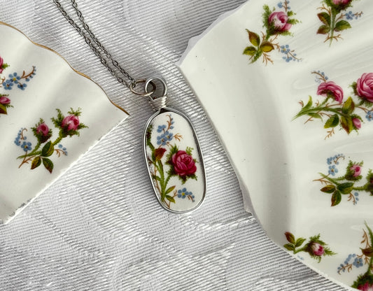 Silver necklace with a floral pendant on a floral fabric background