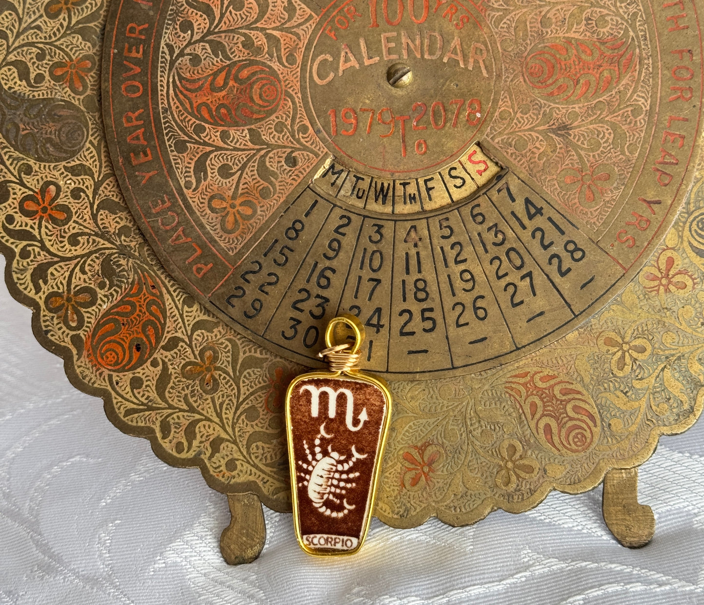 Vintage-style calendar with decorative border and Scorpio pendant on a white background
