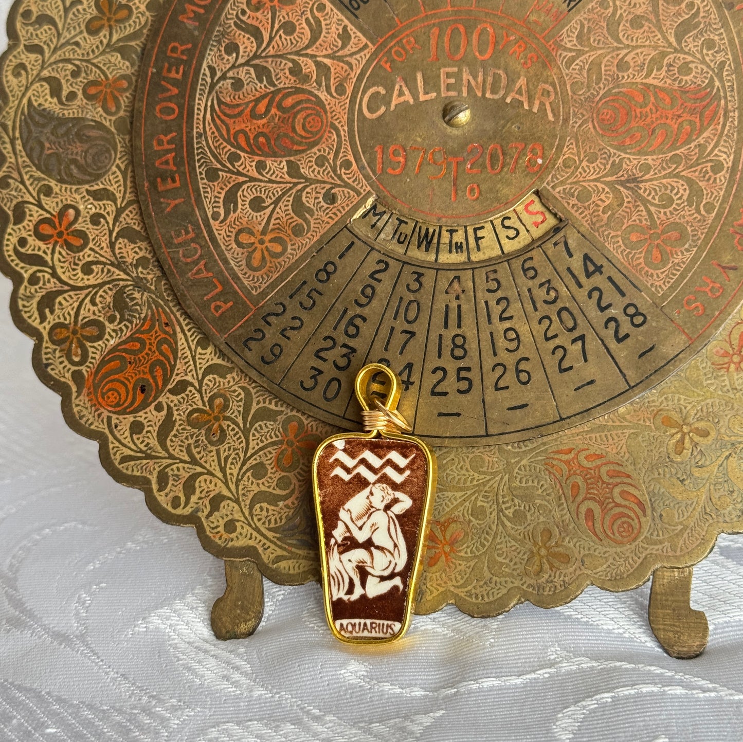 Decorative calendar with aquarius zodiac charm on a white fabric background