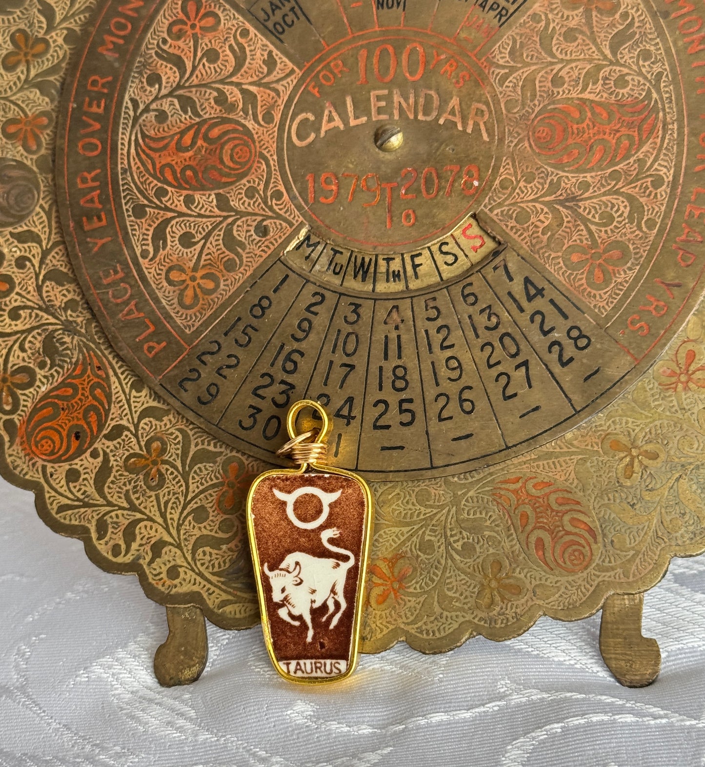 Decorative calendar with tarus zodiac sign pendant on a white fabric background